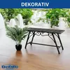 A black metal garden bench with decorative scrollwork is placed on a wooden floor next to a potted artificial plant. The background shows a bright, airy outdoor or conservatory setting with lush greenery and white architectural elements. Náhľad obrázku produktu