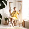 A woman sits in a hanging chair in a well-lit room with blinds casting shadows. Podgląd zdjęcia produktu