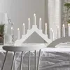 A white candle bridge light is displayed on a table covered with a white tablecloth, with a glass bottle and greenery in the background. Podgląd zdjęcia produktu