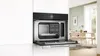 A built-in oven with the door open, showing the interior and a dining room in the background. Anteprima dell’immagine prodotto