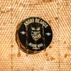 A black jar of beard wax is shown, covered in dripping honey, against a honeycomb background. Produktbild-Vorschau