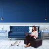A woman is sitting on a folded mattress using a laptop in a living room with blue walls and a blue sofa. Voir les images du produit