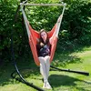 A woman is sitting in a hammock chair outdoors, with green foliage in the background. Podgląd zdjęcia produktu