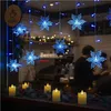 A window display decorated with snowflake-shaped LED lights and faux candles, with people visible inside a cafe. Anteprima dell’immagine prodotto