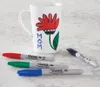 A white mug decorated with a flower and the word "MOM" is shown with four Sharpie permanent markers in red, green, blue, and black. Voir les images du produit