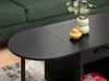 A close-up view of a black coffee table with decorative vases on top, placed in a living room setting next to a green sofa. Náhľad obrázku produktu