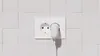 A white electrical outlet with a white USB-C adapter plugged into one of the sockets, set against a white tiled wall. Produktbild-Vorschau
