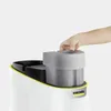 A hand is shown placing a gray water tank onto a white Kärcher device. A yellow trim separates the top section from the main body of the device. Voir les images du produit