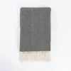 A folded gray herringbone blanket with cream fringe is laid flat on a white background. Anteprima dell’immagine prodotto