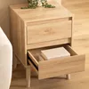 A wooden nightstand with two drawers, one of which is open, revealing books inside. A plant is on top of the nightstand. Podgląd zdjęcia produktu