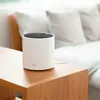 A white cylindrical router sits on a wooden table next to a couch with white pillows. Náhľad obrázku produktu