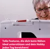 A woman is smiling and looking at a sewing machine. Produktbild-Vorschau