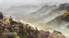 Three people are standing on a rocky outcrop overlooking a vast, misty valley with a river winding through it. The landscape is mountainous and appears to be from a video game. Produktbild-Vorschau