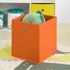 A toy storage cube with a stuffed toy inside, placed on a rug in front of a shelf. Produktbild-Vorschau