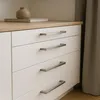 Close-up of a white dresser with silver drawer pulls, a wooden top, and a decorative vase and book. Produktbild-Vorschau