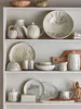 A collection of ceramic kitchenware, including pitchers, teapots, bowls, plates, and a juicer, displayed on shelves. Produktbild-Vorschau