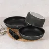 A set of black cookware with water droplets on a textured surface. Produktbild-Vorschau