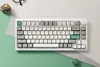 A white mechanical keyboard is displayed on a surface with mint green and light gray geometric shapes. Produktbild-Vorschau