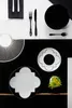 A flat lay of black and white tableware, including plates, cutlery, and a decorative fan-like object. Produktbild-Vorschau