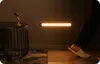 A person's foot wearing a slipper is shown stepping near a wall-mounted light strip in a dimly lit room. Podgląd zdjęcia produktu