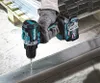 A person wearing gloves is using a Makita cordless drill to drill into a metal beam. Produktbild-Vorschau