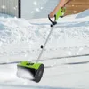 A person is using a green electric snow blower to clear snow from a driveway. Podgląd zdjęcia produktu