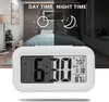A digital alarm clock is shown in front of a split image of a bedroom, depicting day and night. Náhled obrázku produktu