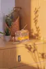 A wooden model tram sits on a wooden surface next to a plant and a basket of flowers, with dappled light and shadows. Produktbild-Vorschau