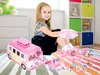 A young girl is playing with a pink toy camper van and camping accessories on a colorful striped rug in a room with shelves in the background. Náhľad obrázku produktu