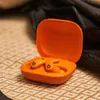 An open orange charging case with two orange earbuds inside, resting on a textured surface. Anteprima dell’immagine prodotto