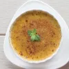 A crème brûlée in a white ramekin, garnished with a mint leaf, sits on a white plate. Produktbild-Vorschau