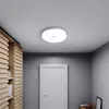 A flush mount LED ceiling light is shown on a white ceiling in a hallway with a wooden cabinet and a white door. Náhľad obrázku produktu