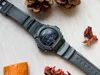 A black Casio digital watch is laid out on a textured beige surface, surrounded by pine cones and dried leaves. Produktbild-Vorschau