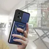 A hand holding a blue phone case with a ring holder and camera cover, with a blurred indoor background. Produktbild-Vorschau