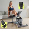 A woman is exercising on a recumbent exercise bike in a living room setting. Produktbild-Vorschau