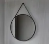 A round mirror with a black frame and a black strap hanging on a textured gray wall. Anteprima dell’immagine prodotto