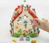 A wooden toy house with various educational features, including number shapes and a xylophone, against a white background. A hand is shown inserting a number '3' into the house. Náhľad obrázku produktu