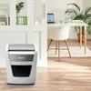 A Leitz shredder is shown in a modern office setting next to a desk with a laptop and a plant. Náhľad obrázku produktu