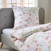 A close-up view of a bed with white bedding featuring a floral pattern. Produktbild-Vorschau