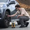 A man is using a portable air compressor to inflate a car tire. Podgląd zdjęcia produktu