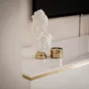 A white bust of a woman on a gold base sits on a white shelf next to a small gold jar. Produktbild-Vorschau