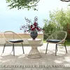 Two wicker chairs and a table with a flower arrangement on a rug outdoors, with a view of the sea in the background. Produktbild-Vorschau