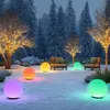 A snowy garden scene at dusk, illuminated by colorful solar garden lights and string lights on trees. Produktbild-Vorschau