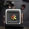 A square black plate with a meal is set on a dark wooden table, with cutlery and a glass of red wine. Náhled obrázku produktu