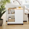 A white rolling cabinet with a wooden top sits next to a white sofa, with a plant in the foreground. Náhľad obrázku produktu