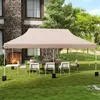 A beige canopy tent set up on a grassy lawn in front of a stone building, with a table and chairs underneath. Náhled obrázku produktu