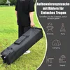 A person is carrying a black storage bag with wheels on a grassy field. The bag is likely for a pop-up tent or pavilion. Voir les images du produit