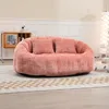 A plush pink loveseat sits on a checkered rug in a well-lit room.