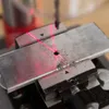 A close-up of a drill press with a laser guide focused on a metal workpiece held in a vise. Produktbild-Vorschau