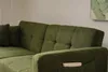 A close-up view of a green sofa with tufted back cushions and a small wooden object tucked into a side pocket. Produktbild-Vorschau